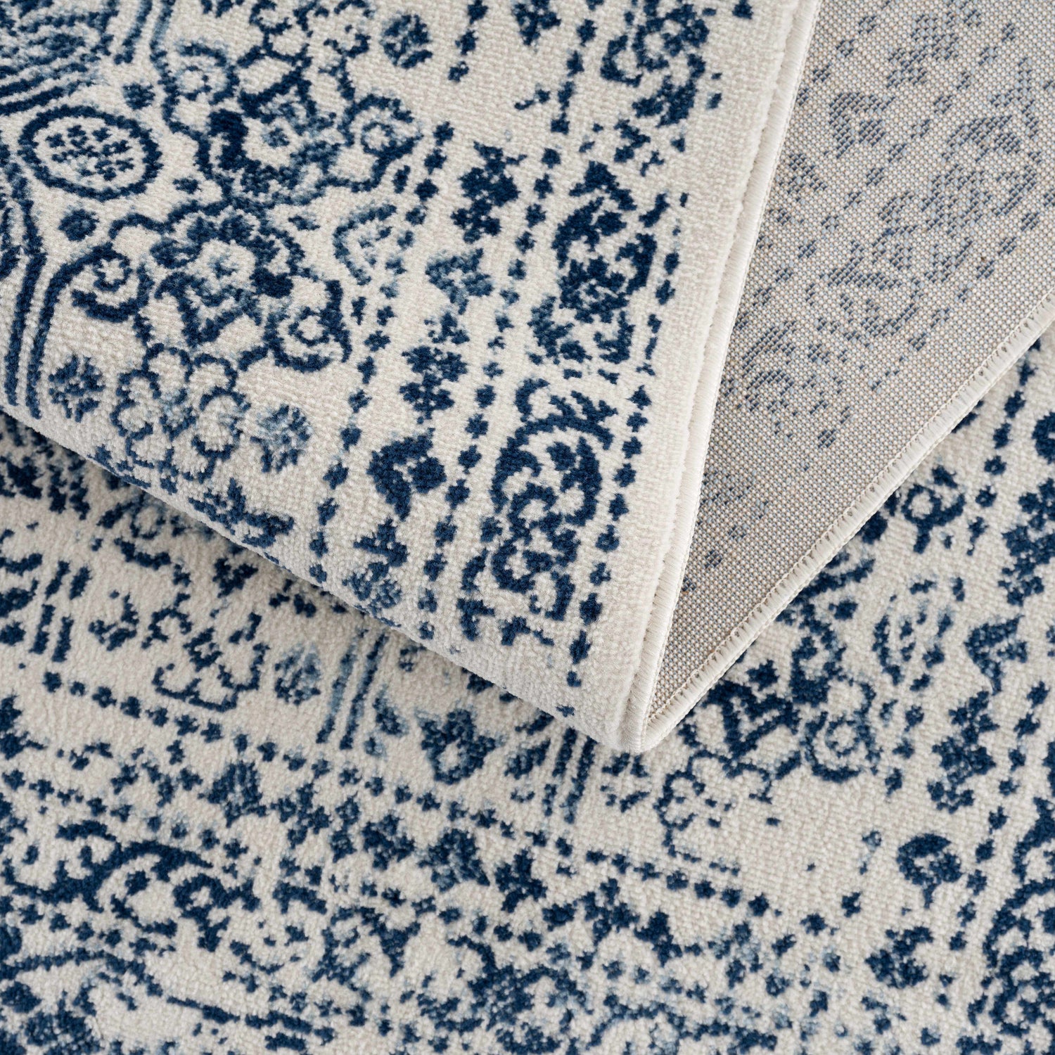 Close-up of the Michie Blue Area Rug showing its dark and light blue bohemian pattern on a white background. Fold