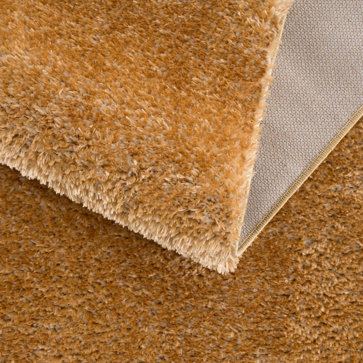 Close-up of the Heavenly Solid Mustard Plush Rug showing its shag texture and backing. Fold