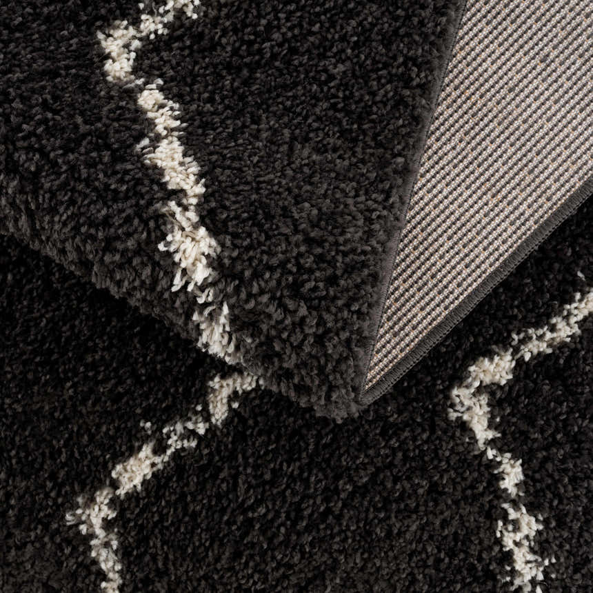Close-up of the Ennis Area Rug, a charcoal shag rug with a light beige Berber pattern and woven backing. Fold
