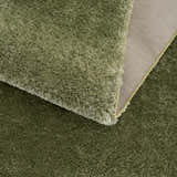 Close-up of the plush Heavenly Solid Green Rug showing its shag texture and backing. Fold