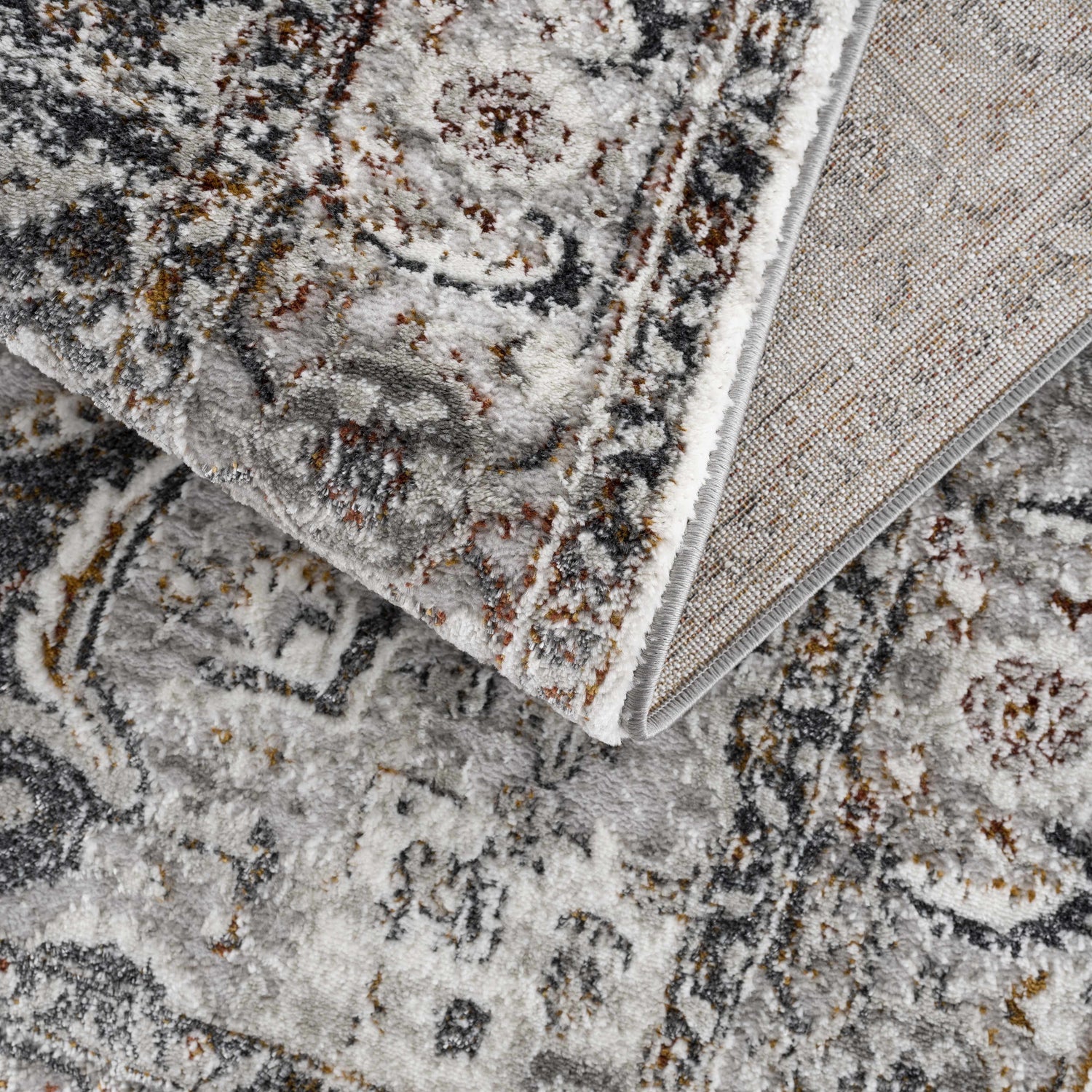 Close-up of the Liverpool Dark Gray Area Rug showing its charcoal, gray, rust, and off-white traditional design. Fold