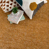Close-up of the Heavenly Solid Mustard Plush Rug with books and textured throw pillows. Styleshot