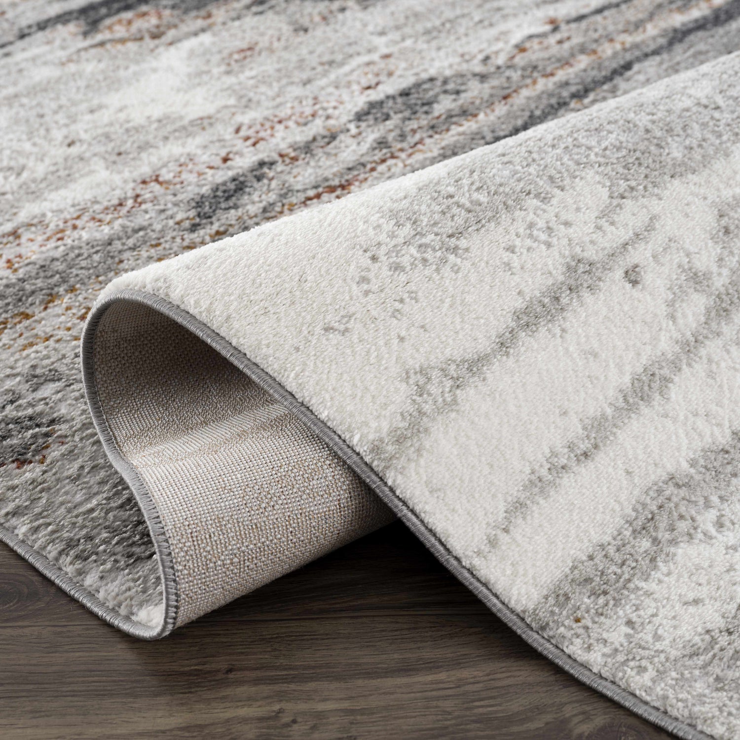 Close-up of the Live Marble Gray Area Rug showing its charcoal, rust, and gray abstract pattern and soft texture. Fold