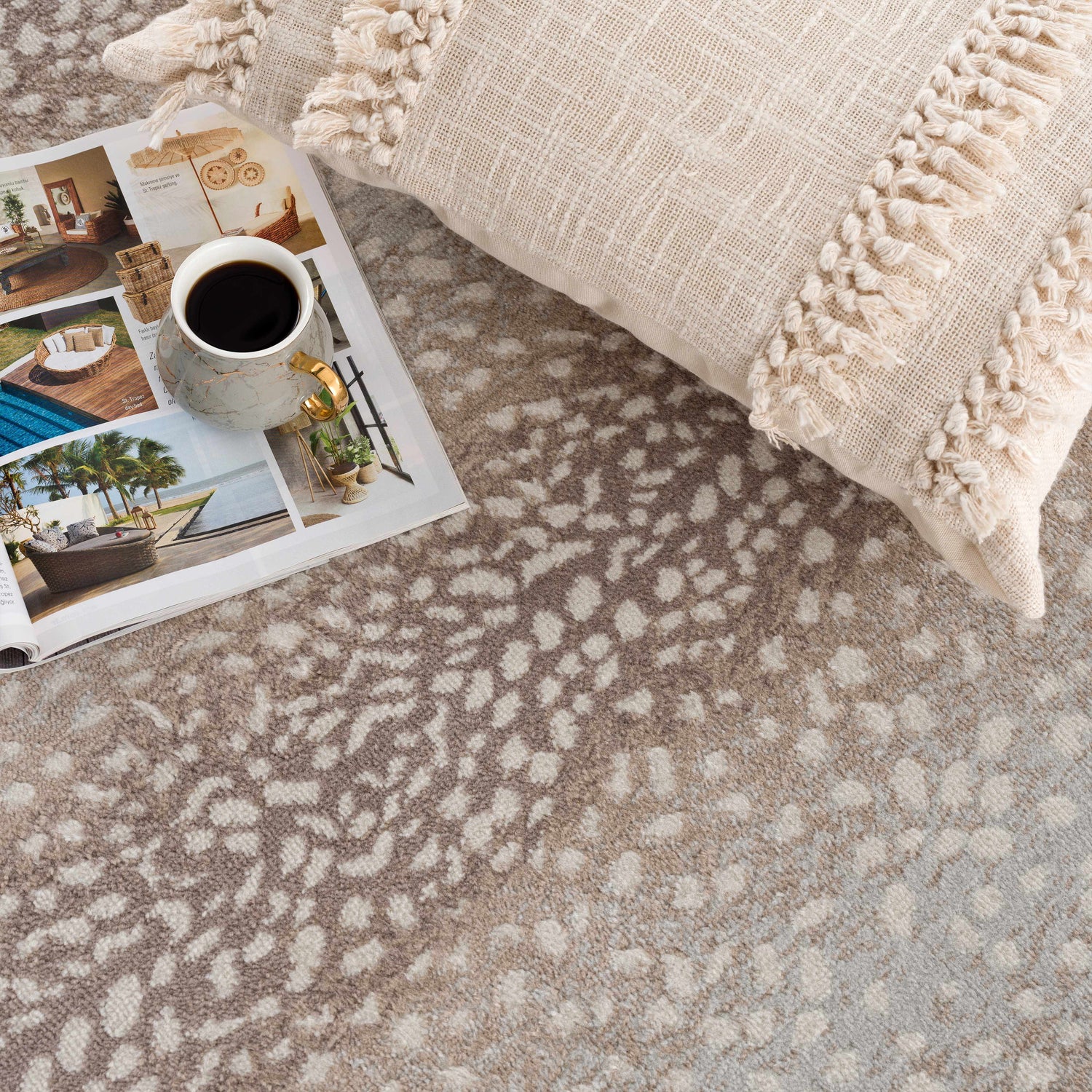 Close-up of Pointblank Tan Leopard Print Rug with ivory pillow and magazine, showcasing the rug's animal print design. Styleshot