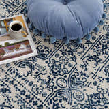 Close-up of the Michie Blue Area Rug showing its dark blue and white bohemian pattern, with a blue pompom pillow. Pile