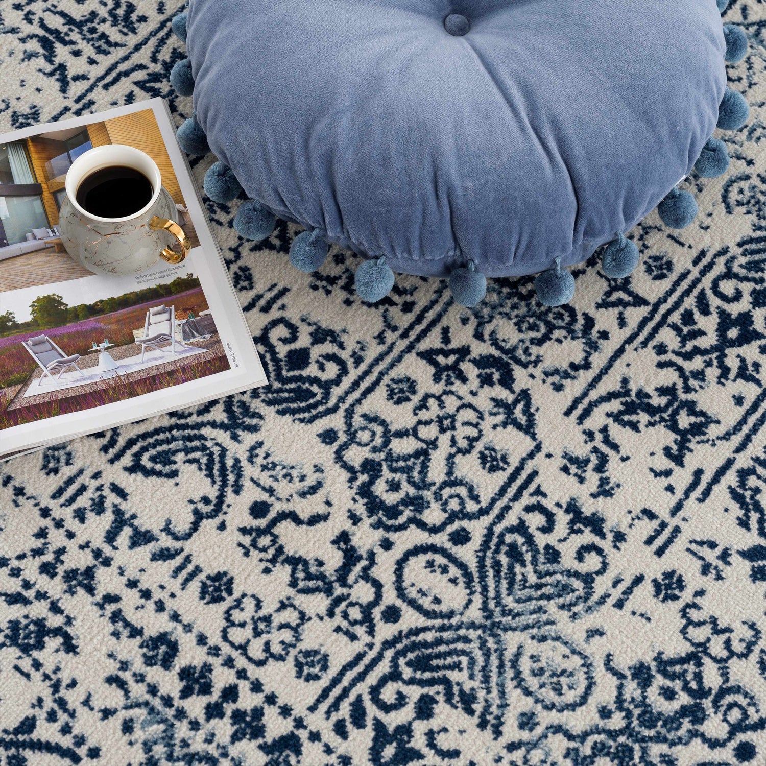 Close-up of the Michie Blue Area Rug showing its dark blue and white bohemian pattern, with a blue pompom pillow. Pile