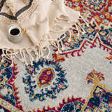 Close-up of the Istanbul Medallion Orange Area Rug, showcasing its ivory base and colorful bohemian medallion pattern. Coffee cup and throw. Styleshot