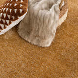 Close-up of the Heavenly Solid Mustard Plush Rug showing texture, with a throw blanket, patterned pillow, and woven basket. Styleshot