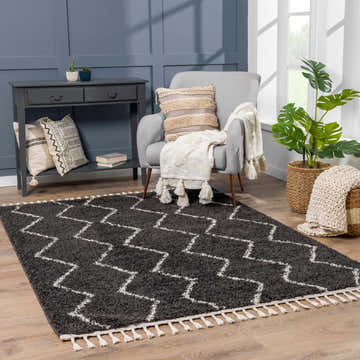 Living room scene with gray armchair, console table, and charcoal Ennis Area Rug with light beige zigzags and tassels. Roomscene-Rectangle