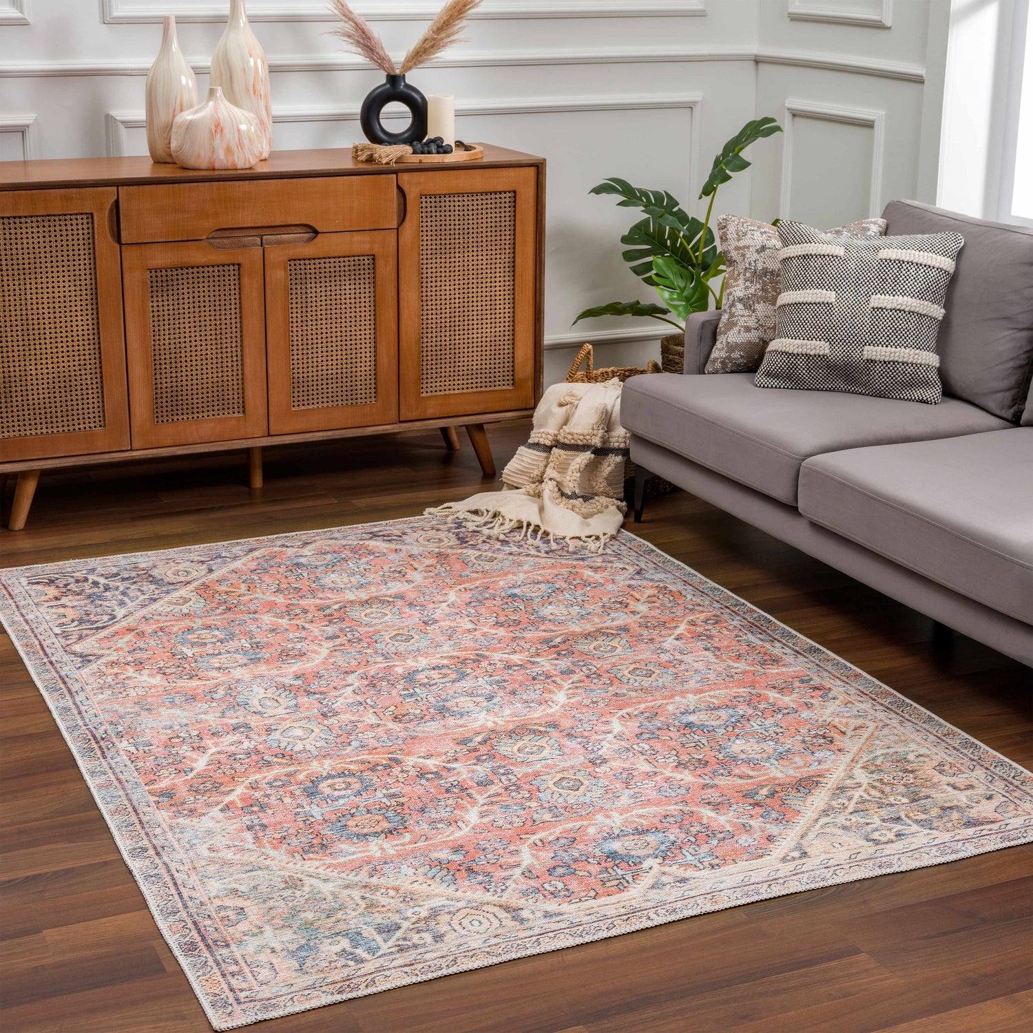 Living room scene with a Konstantina Washable Area Rug in peach, blue, and beige, styled with a gray sofa and wood cabinet. Roomscene-Rectangle