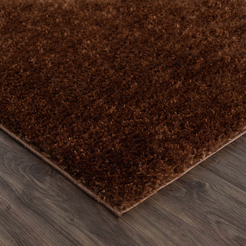 Close-up of the plush Heavenly Solid Brown Rug showing its texture and color on dark wood flooring. Corner