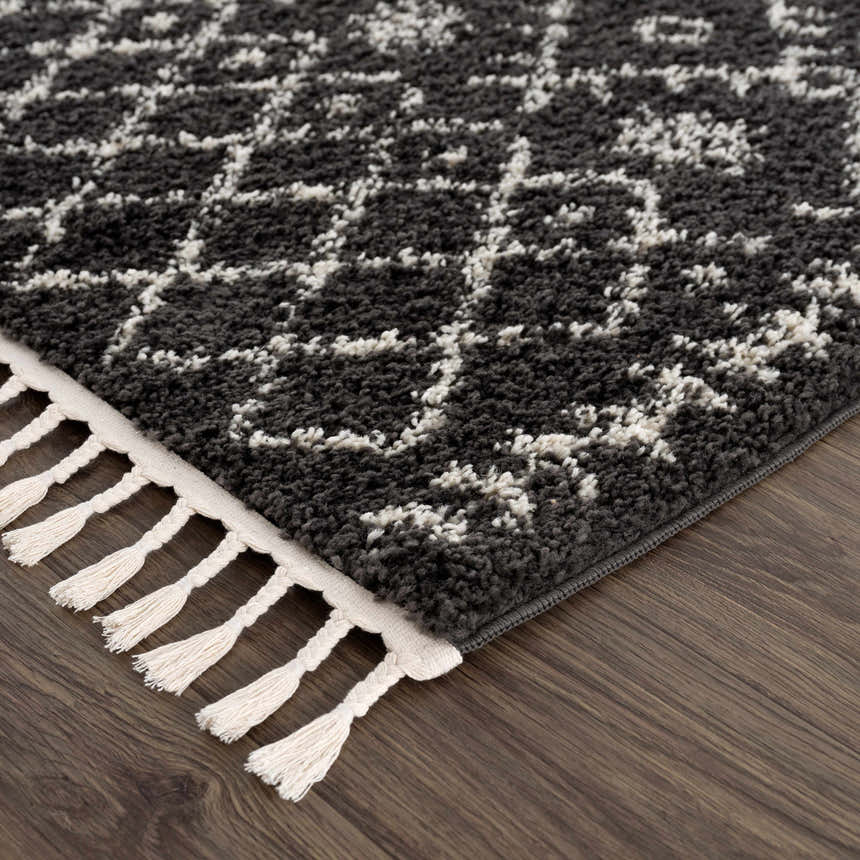 Close-up of the Thetford Black Berber Shag Rug showing charcoal and light beige geometric pattern and fringe detail. Corner