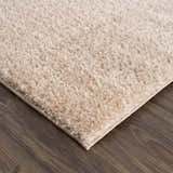 Close-up of the plush Heavenly Dark Beige Area Rug showing its shag texture and color on a dark wood floor. Corner