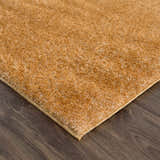 Close-up of a Heavenly Solid Mustard Plush Rug showing its soft texture and color on dark wood flooring. Corner