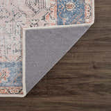 Close-up of the Rosman Distressed Washable Area Rug showing beige, blue, and pink oriental pattern and gray backing on wood floor. Fold
