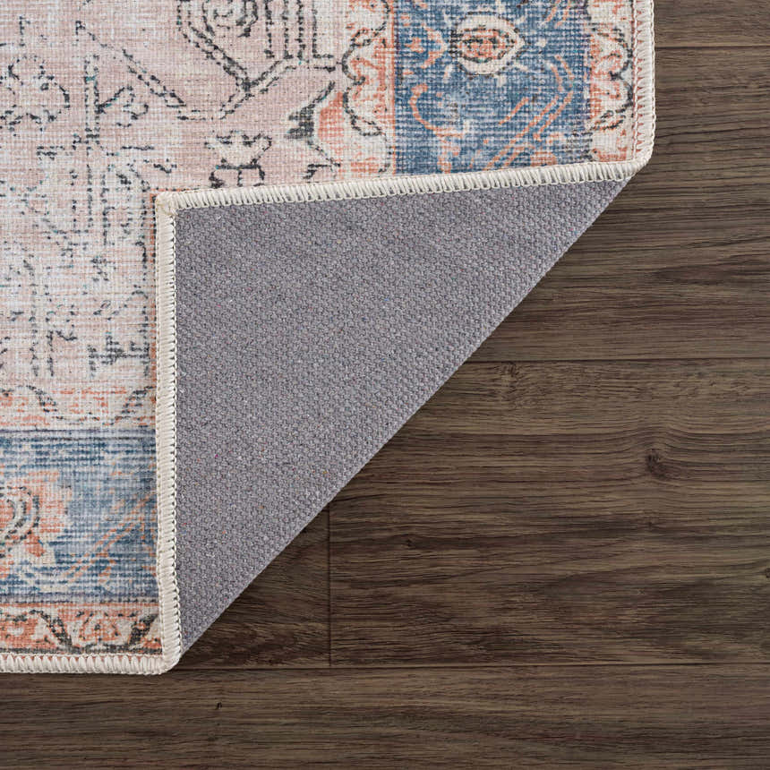 Close-up of the Rosman Distressed Washable Area Rug showing beige, blue, and pink oriental pattern and gray backing on wood floor. Fold