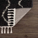 Close-up of the Berber Shag Ennis Area Rug in charcoal and light beige with tassels, showing the rug's backing. Fold