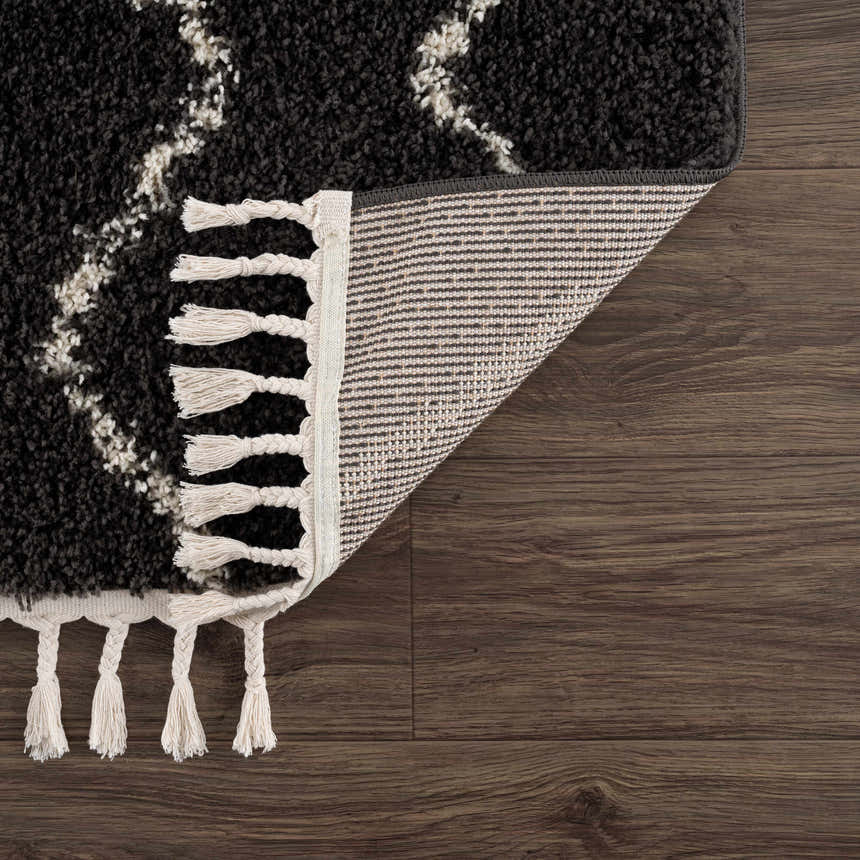 Close-up of the Berber Shag Ennis Area Rug in charcoal and light beige with tassels, showing the rug's backing. Fold