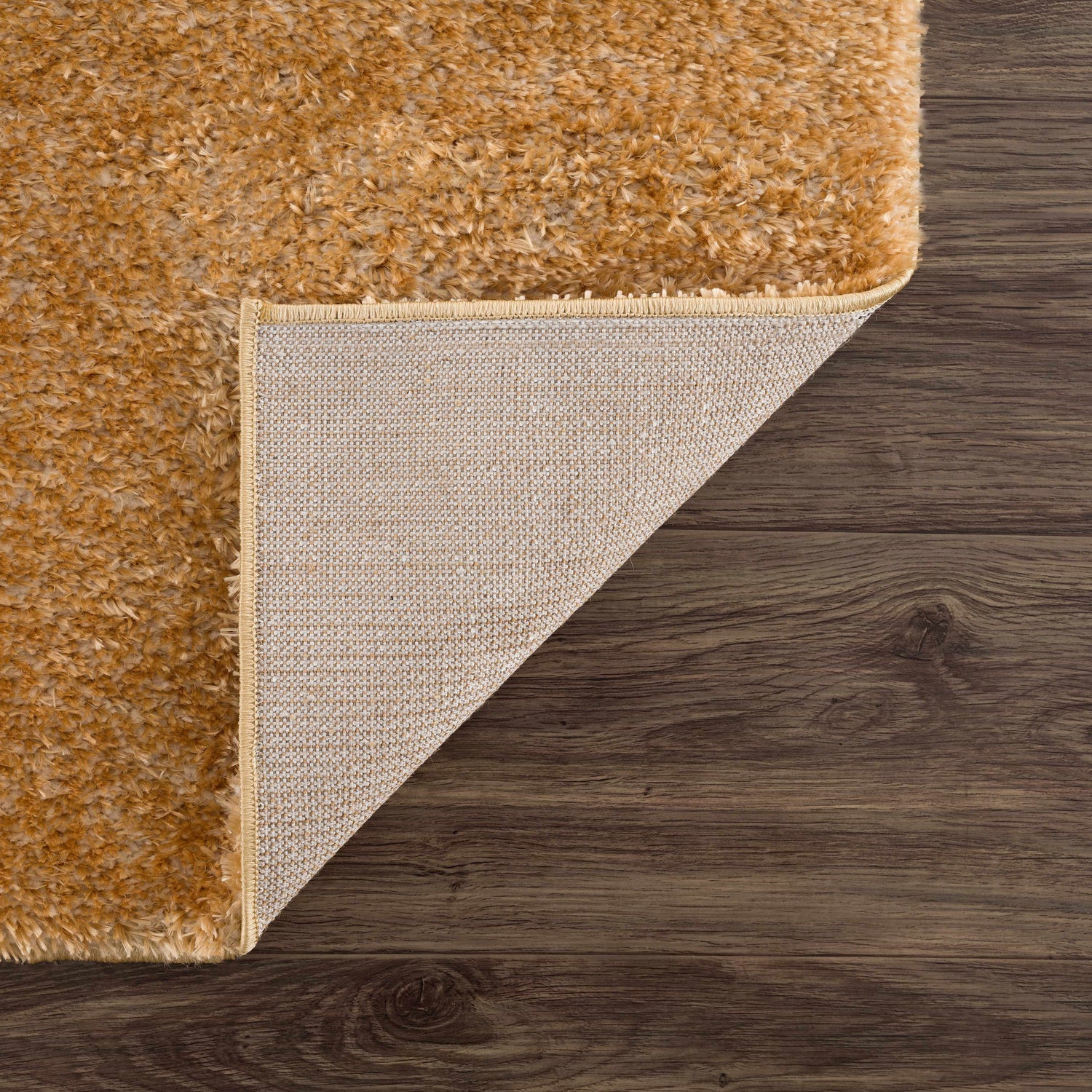 Close-up of Heavenly Solid Mustard Plush Rug showing texture, backing, and edge on a dark wood floor. Fold