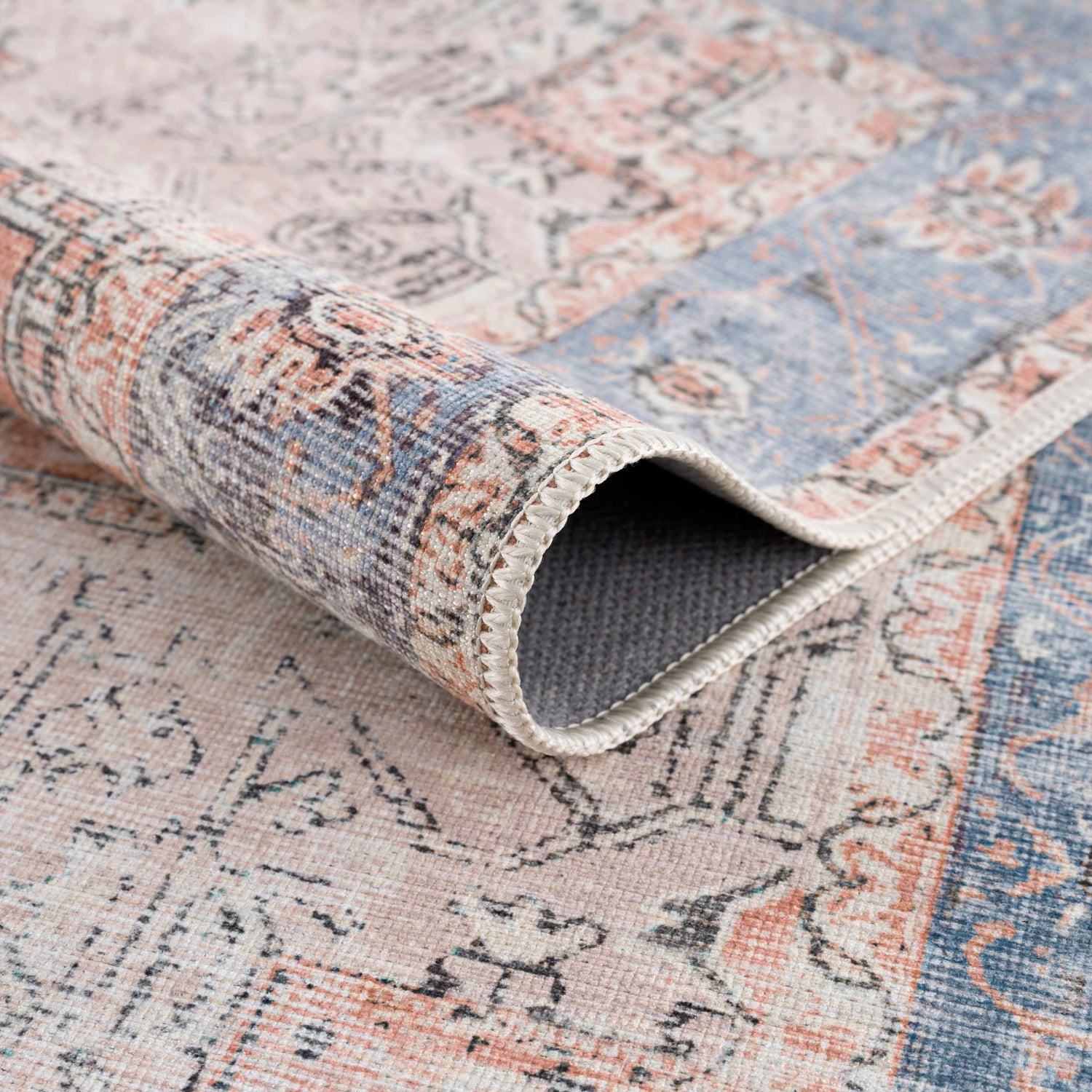Close-up of the Rosman Distressed Washable Area Rug showing its beige, blue, and brick red oriental pattern and soft chenille texture. Fold