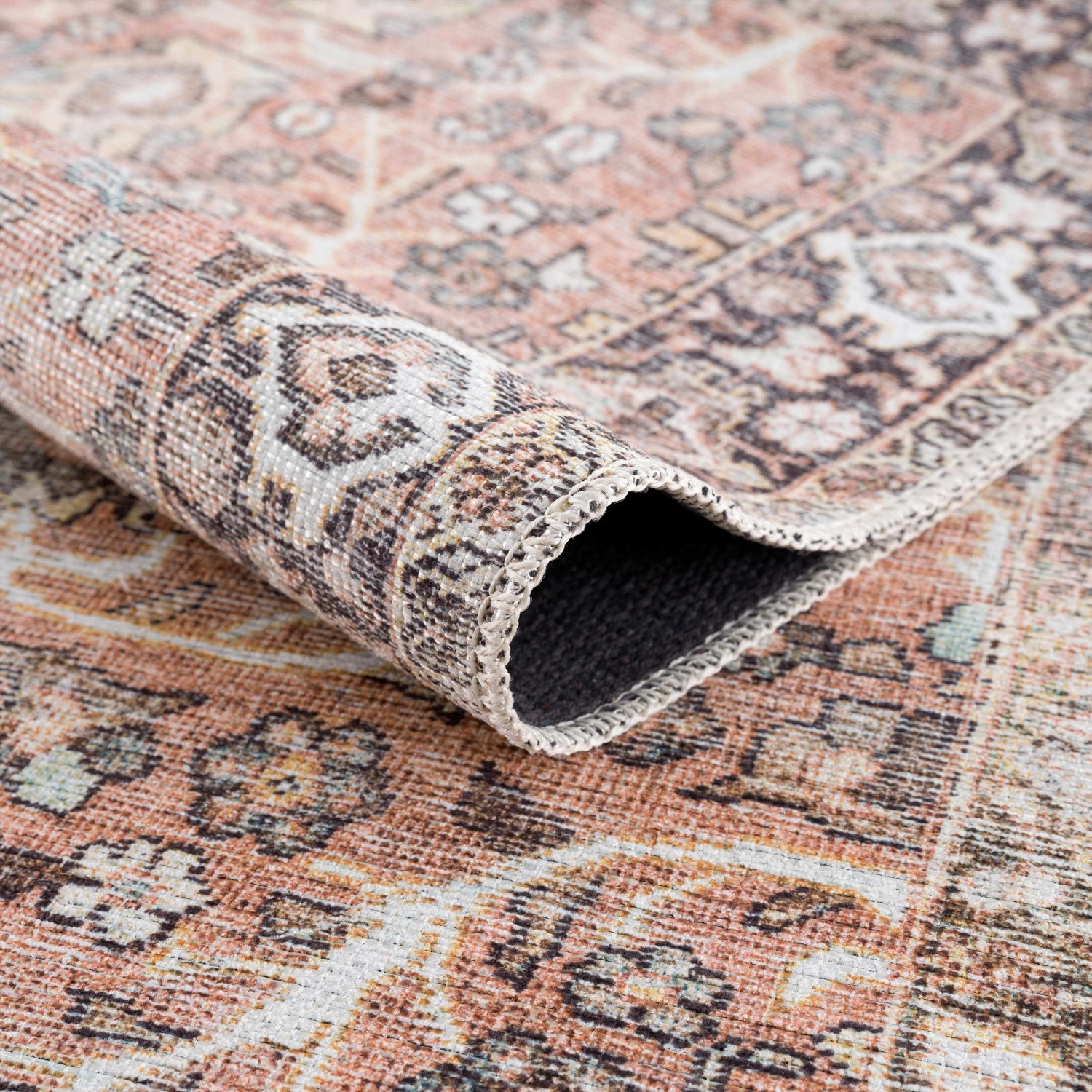 Close-up of a Bian Washable Area Rug. Features a vintage Persian design in aqua, beige, and rose cream hues. Fold
