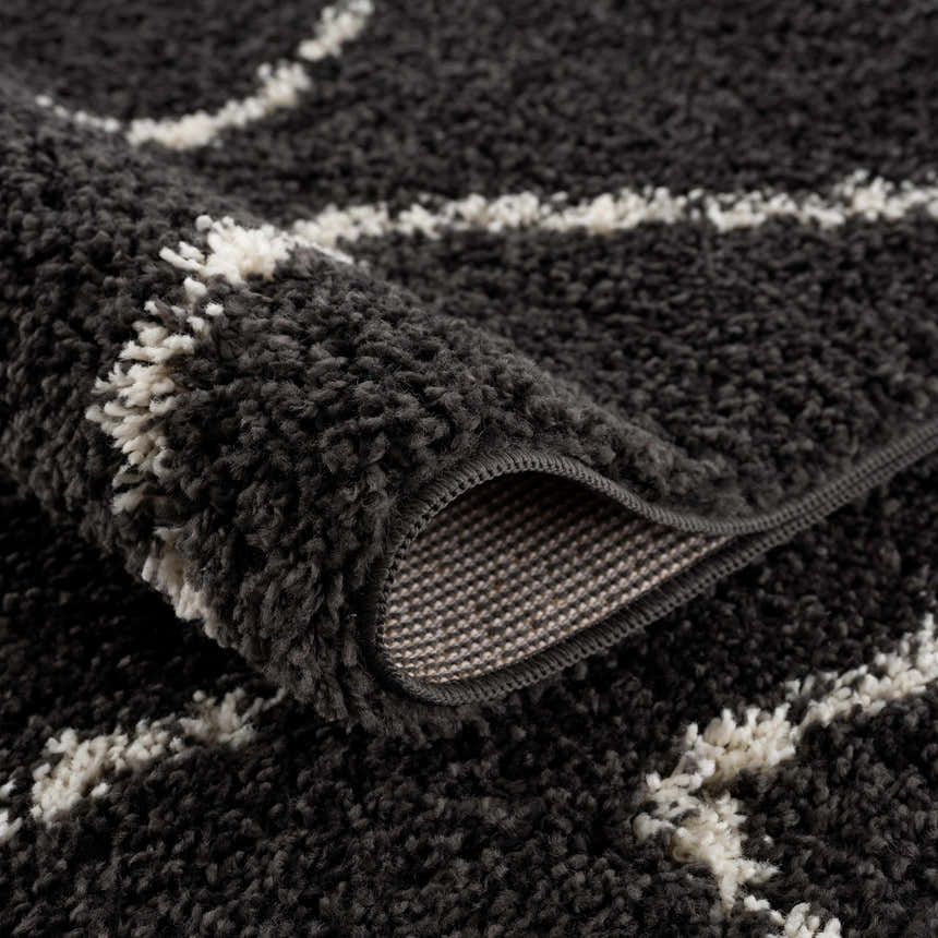 Close-up of the charcoal Ennis Area Rug with a light beige geometric pattern and a soft, shag texture. Fold