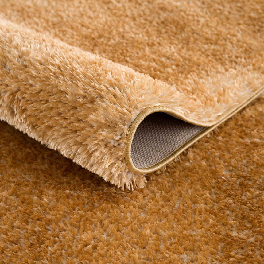 Close-up of the Heavenly Solid Mustard Plush Rug showing its soft, shag texture and bound edge. Fold