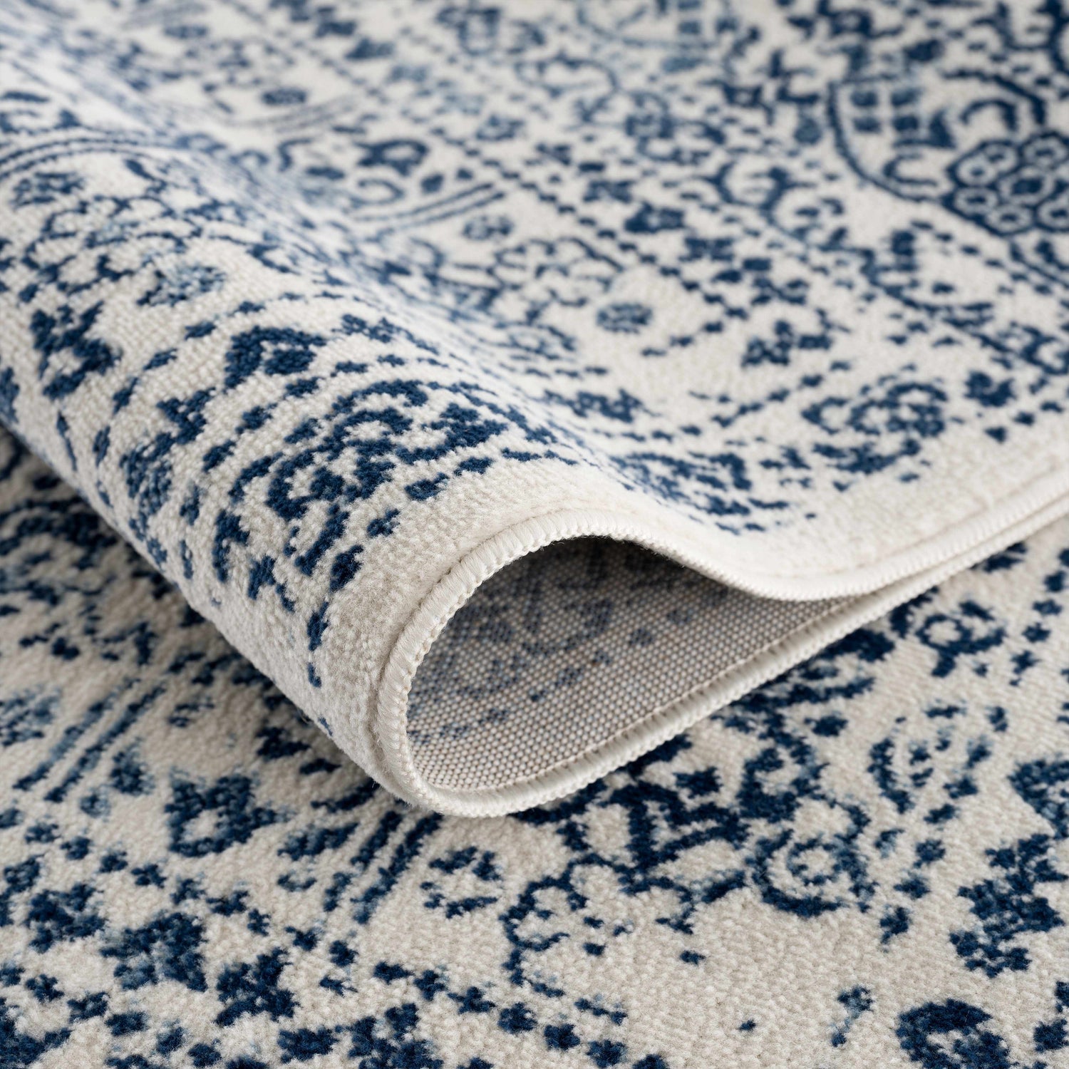 Close-up of the Michie Blue Area Rug showing its dark blue and white bohemian pattern and machine woven texture. Fold