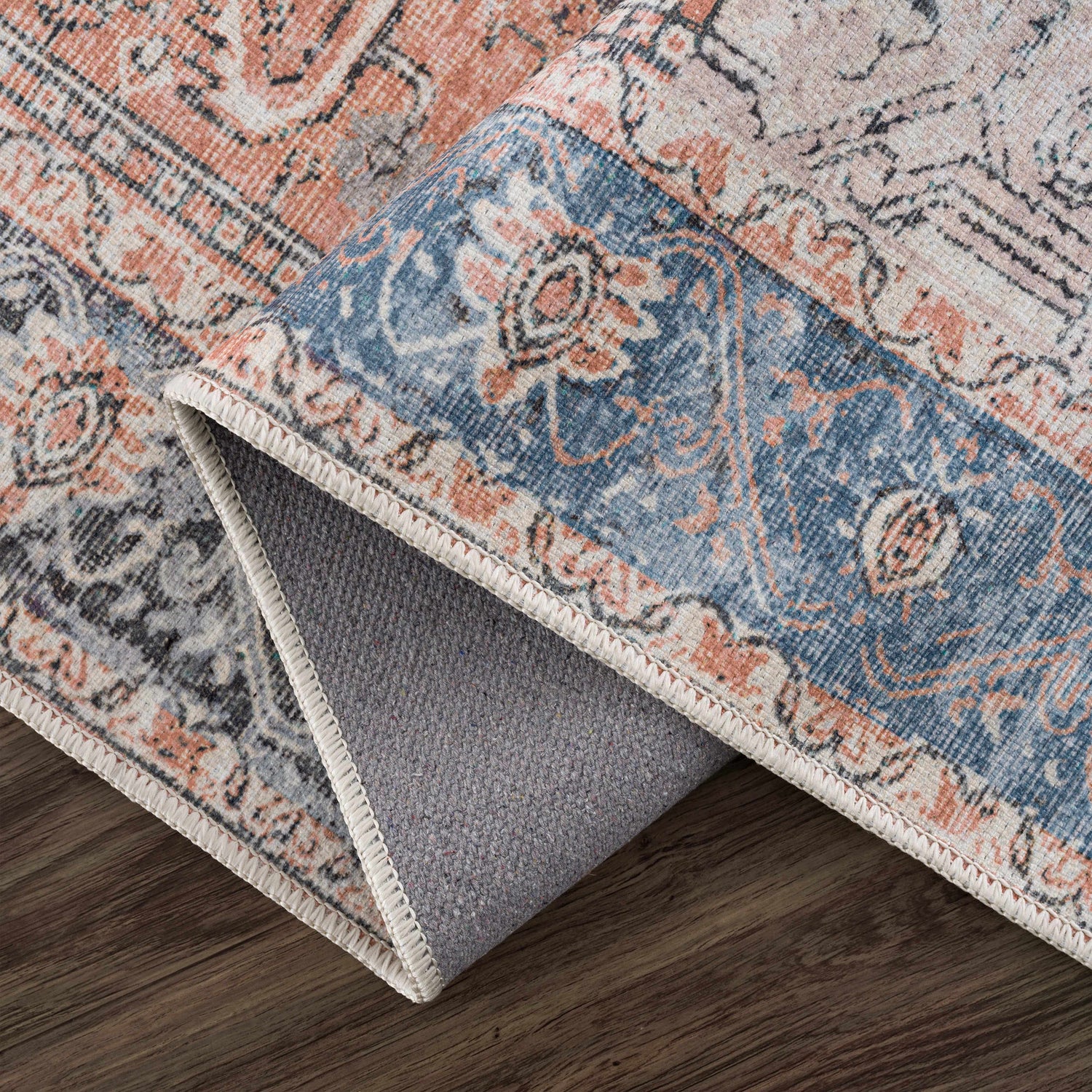 Close-up of the Rosman Distressed Washable Area Rug showing its beige, blue, and brick red oriental pattern and chenille texture. Fold
