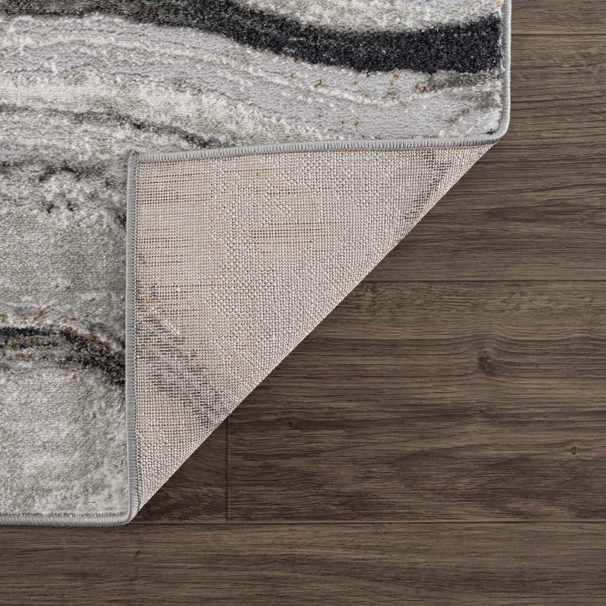 Close-up of Live Marble Dark Gray Area Rug showing charcoal, gray, and rust hues on wood floor with rug backing. Fold