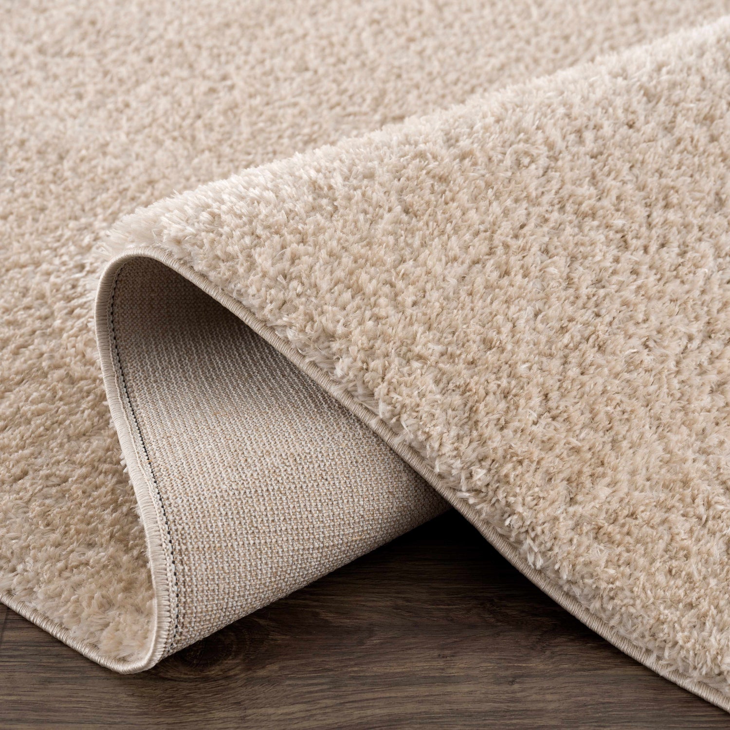 Close-up of the Heavenly Dark Beige Area Rug showing its plush shag texture and durable backing on a wood floor. Fold