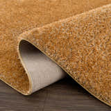 Close-up of a Heavenly Solid Mustard Plush Rug showing its shag texture and backing on a dark wood floor. Fold