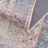 Close-up of the Rosman Distressed Washable Area Rug showing its beige, blue, and brick red oriental pattern and gray backing. Fold