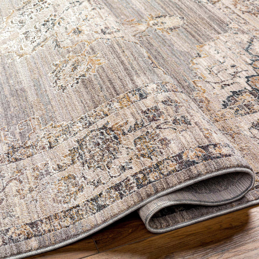 Close-up of the Cream Brown Zola Area Rug showing its traditional pattern, beige, tan, and charcoal colors, and soft polyester texture. Fold