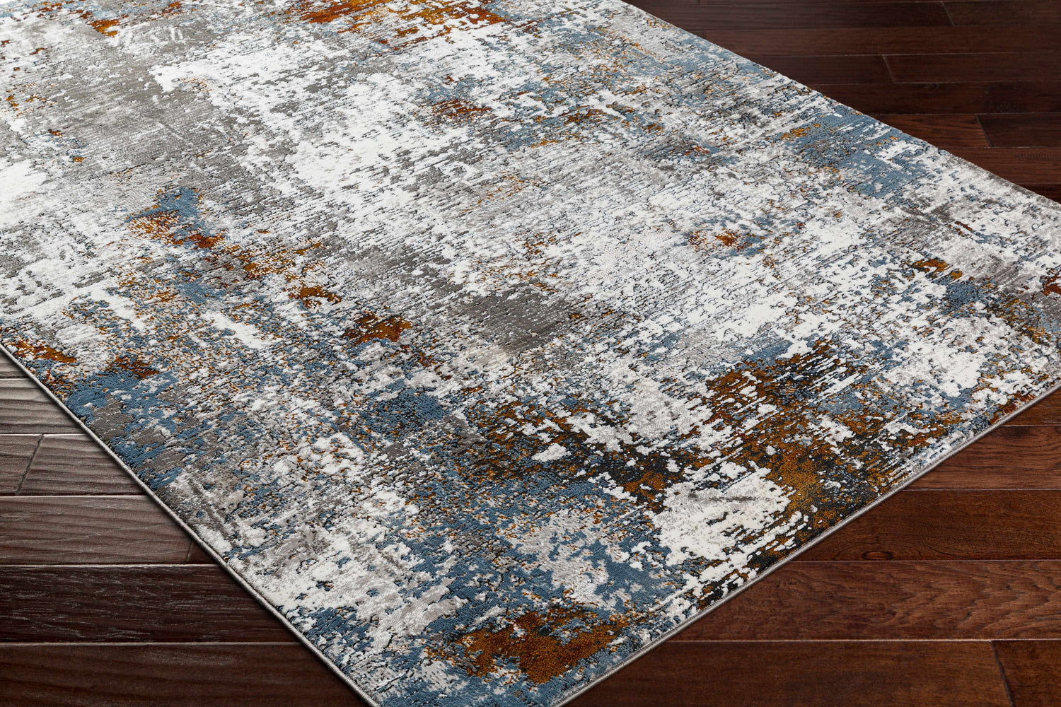 Close-up of the Ansel Area Rug showcasing its abstract pattern in ivory, gray, blue, and rust on a dark wood floor. Corner