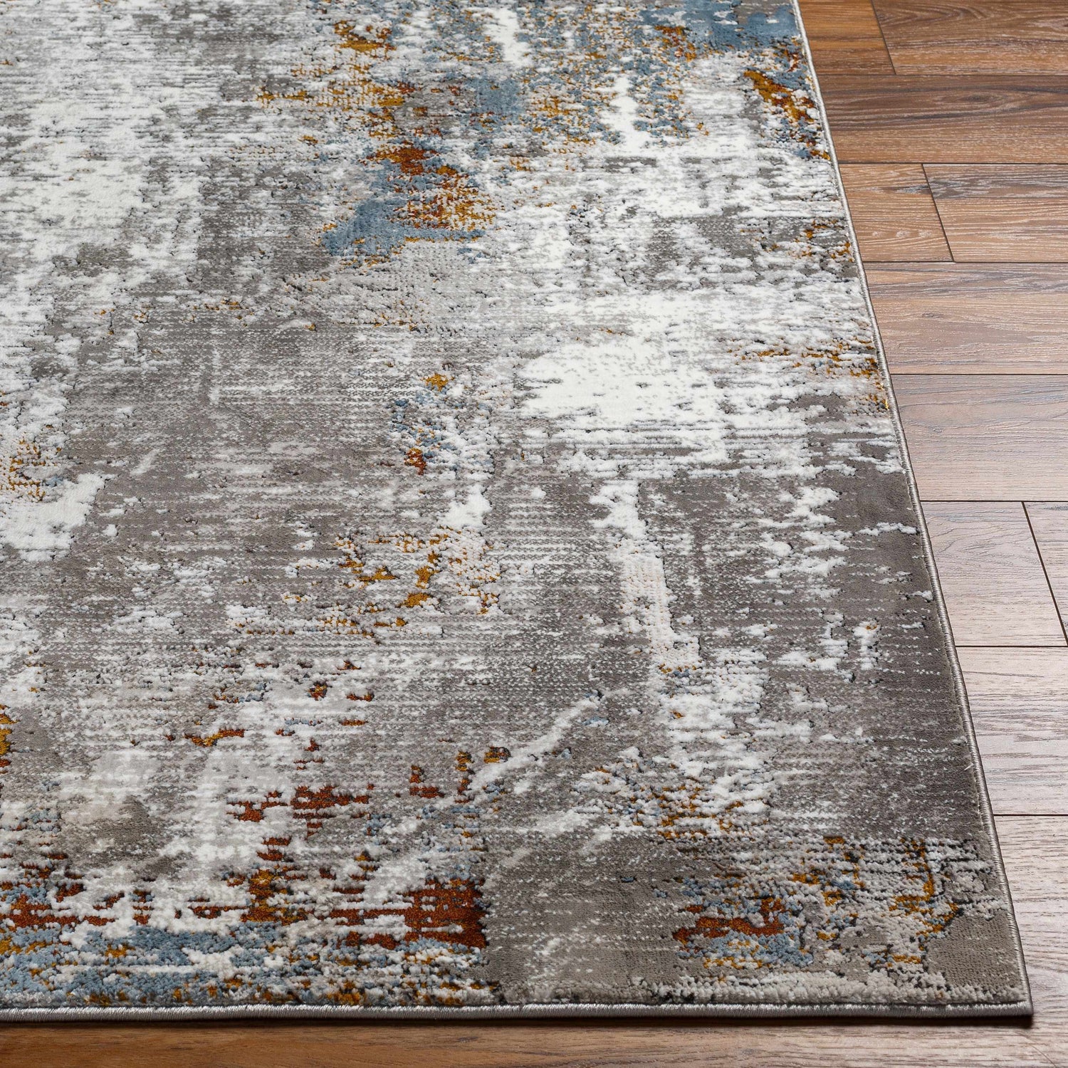 Close-up of the Ansel Area Rug showing a gray, white, rust, and blue abstract pattern on a wood floor. Front