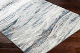Close-up of the Glain Gray & Blue Marble Area Rug showing its abstract pattern and colors on dark wood flooring. Corner