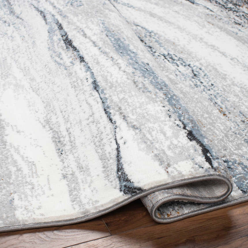 Close-up of the Glain Gray & Blue Marble Area Rug. Features a marble-like pattern in arctic stone, gray, and blue hues. Southwestern style. Fold