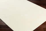 Close-up of a textured Lambswool Kini Plush Washable Rug on dark wood flooring. Corner