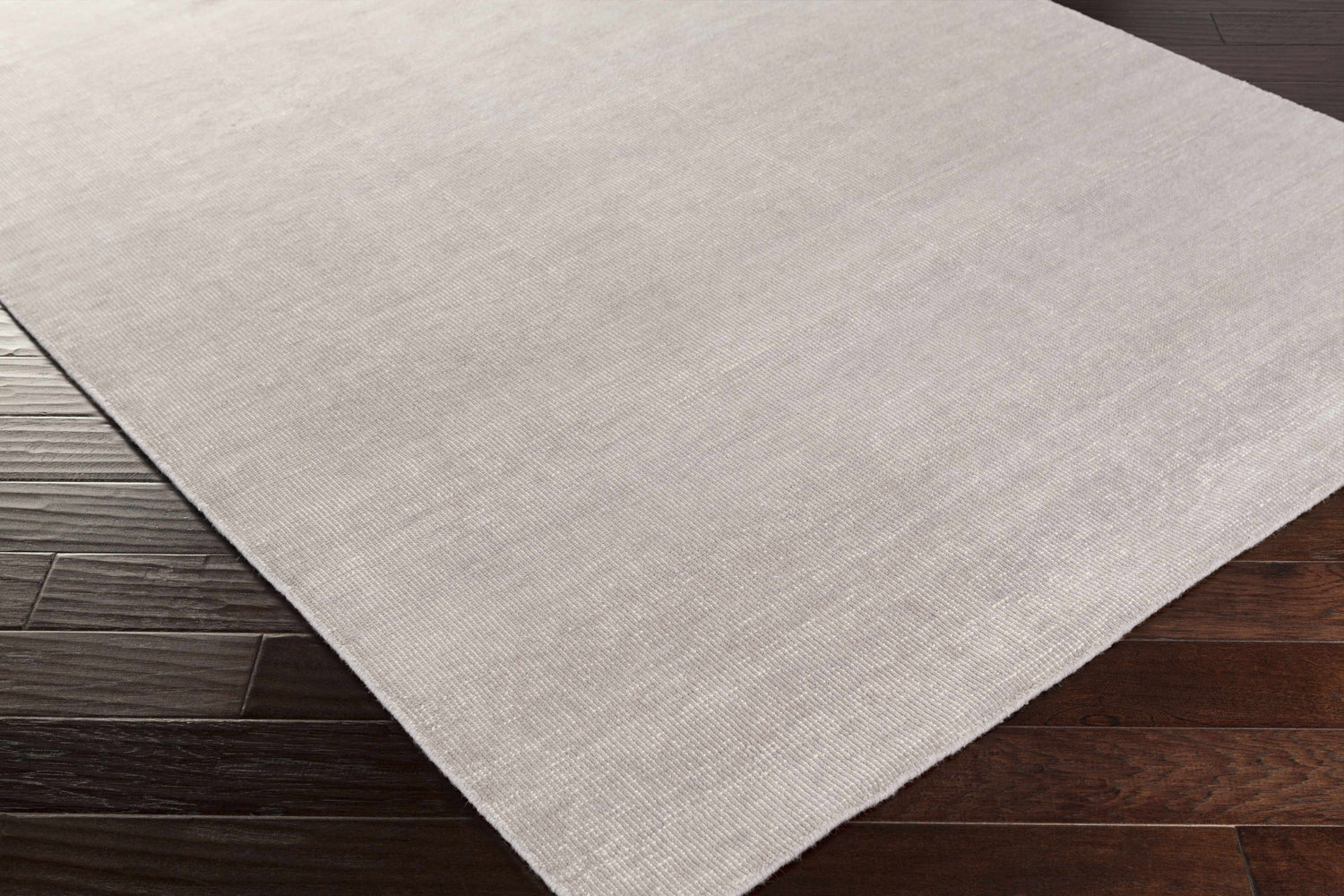 Close up of the gray Salvisa Area Rug showing its hand knotted wool texture on dark wood floor. Corner