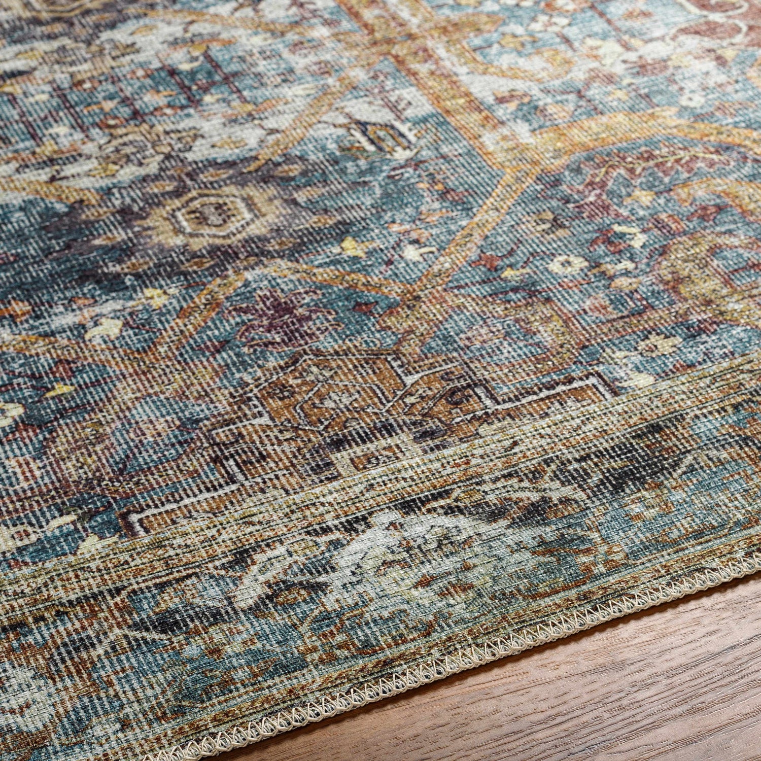 Close-up of the Kaif Washable Area Rug in teal, brown, and cream. Traditional, machine-woven design and textured polyester material. Texture