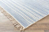 Close-up of the Sanc Blue/Cream rug showing its flatweave texture, geometric pattern, and fringe detail on a wood floor. Front