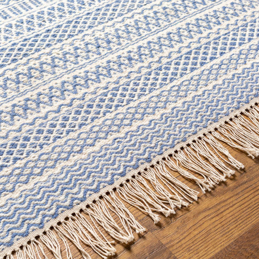 Close-up of the Sanc Blue/Cream rug showing its flatweave texture, geometric pattern, and fringe detail on a wood floor. Texture