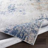 Close-up of the Sapcote Textured Luxe Area Rug showing its charcoal, blue, and beige abstract pattern and textured weave. Fold