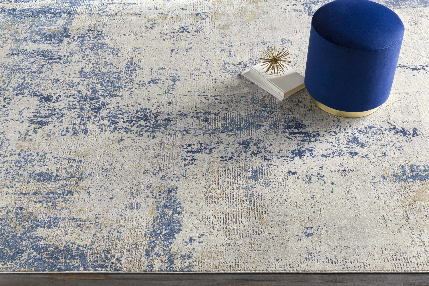 Close-up of the Sapcote Textured Luxe Area Rug in light beige and blue. Features a blue ottoman and decorative accents. Styleshot