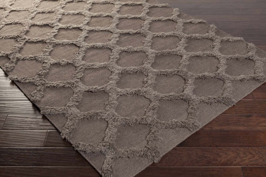 Close-up of the charcoal Saulsville Area Carpet. This hand-woven wool rug features a geometric shag design on dark wood floors. Corner