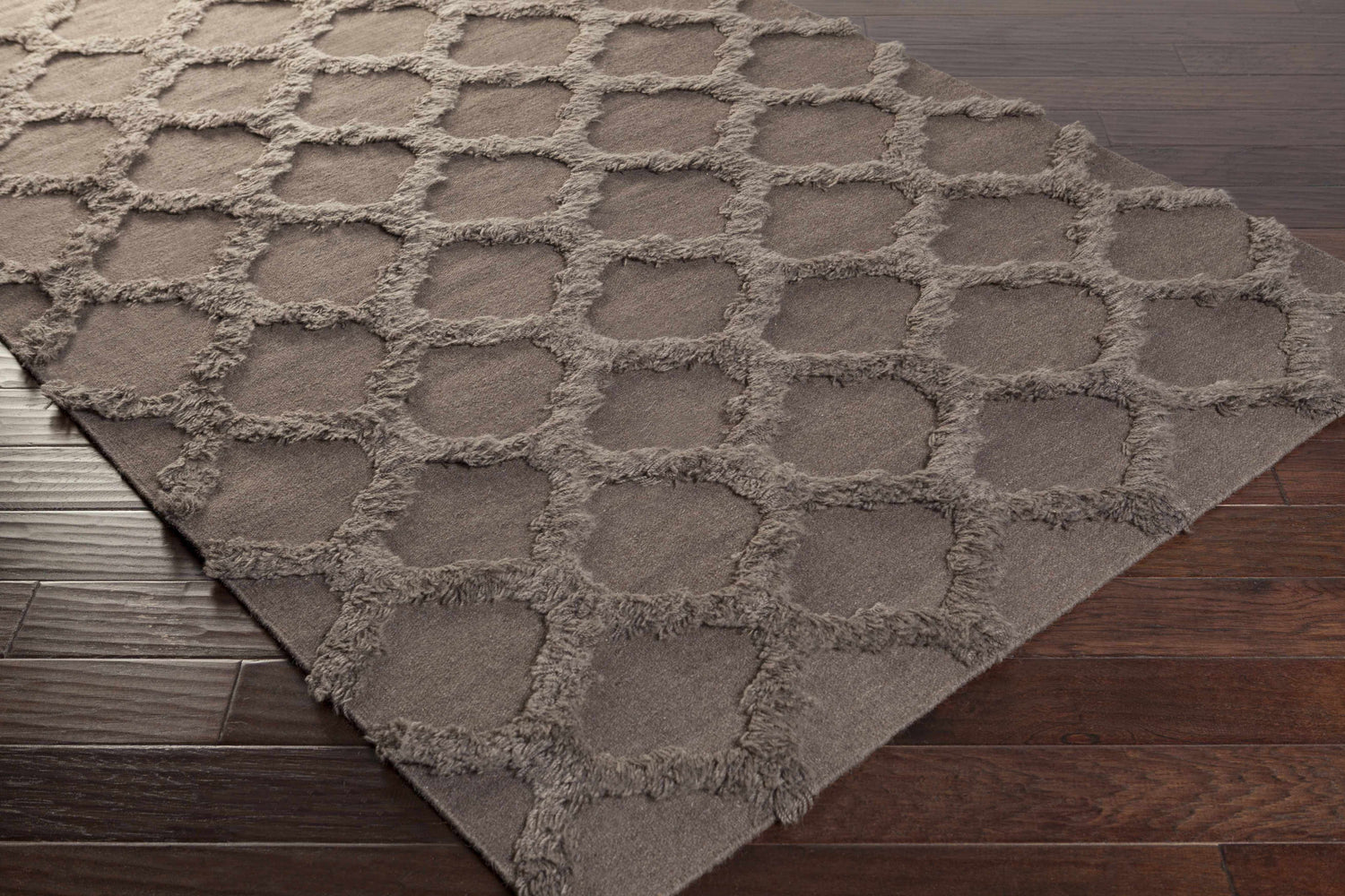 Close-up of the charcoal Saulsville Area Carpet. This hand-woven wool rug features a geometric shag design on dark wood floors. Corner