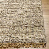 Close-up of the Tan Gopi Area Rug. Hand-woven jute and wool rug with a textured, speckled design and fringe detail. Front