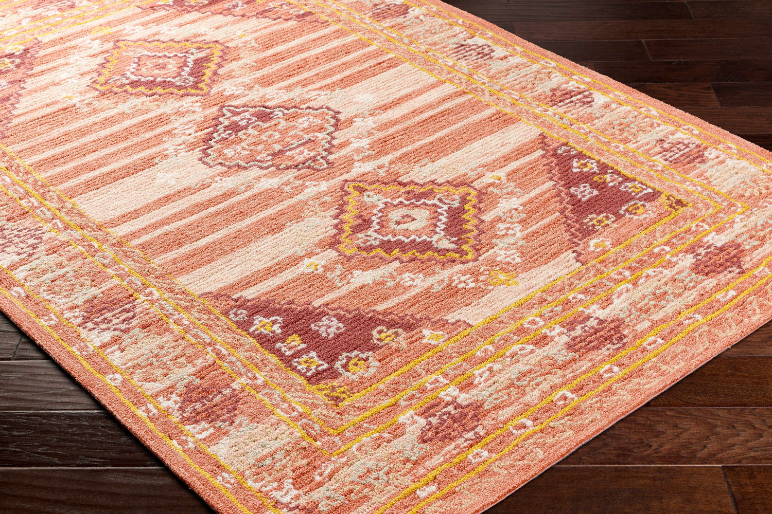 Close up of the hand-tufted Alena Peach Wool Blend Area Rug, featuring bronze, orange, and brown farmhouse-style patterns. Corner