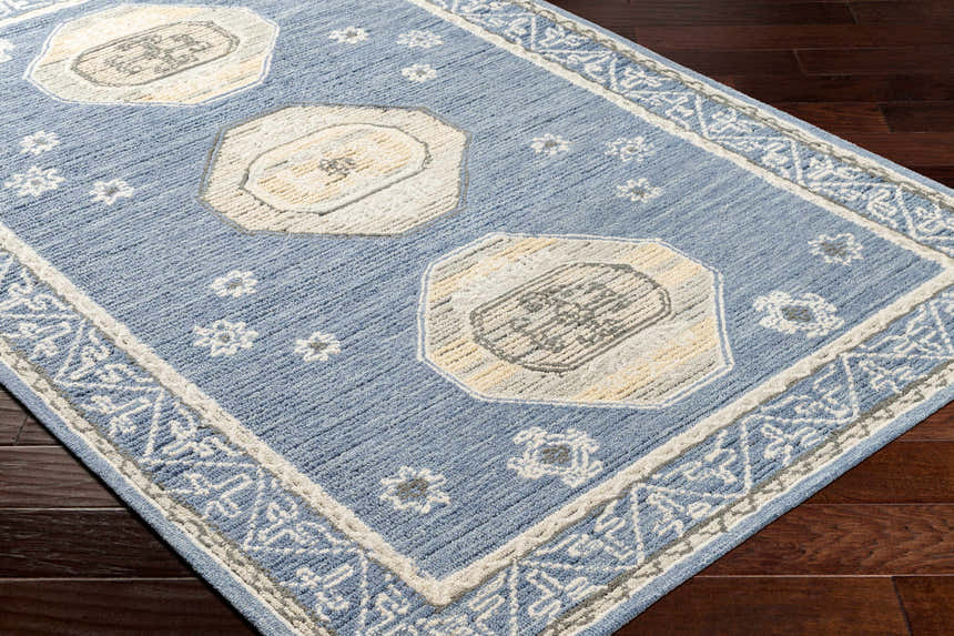 Close-up of the hand-tufted Arwan Area Rug. Farmhouse style with beige, gray, and blue floral and geometric patterns. Corner